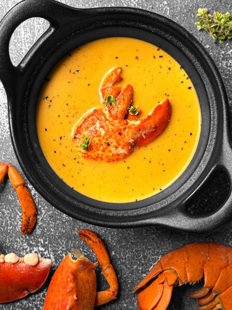 Bisque de homard dans un bol noir, avec pinces de homard en décoration